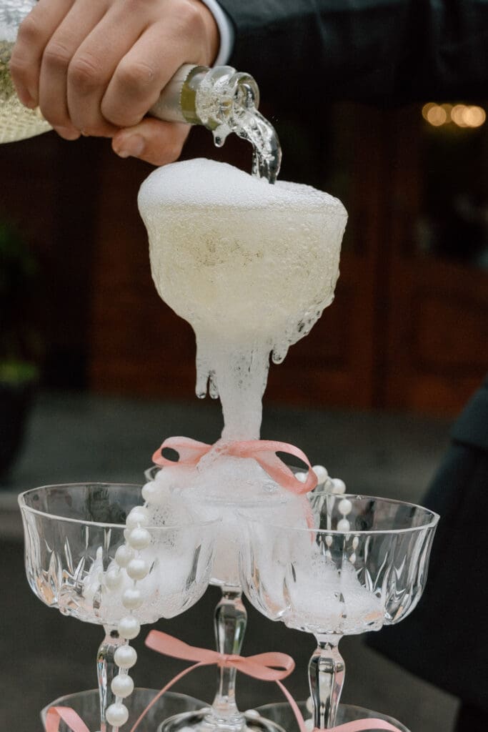 Close-up of champagne tower overflowing as groom pours wine during editorial wedding at Rivers Edge Resort Manitoba