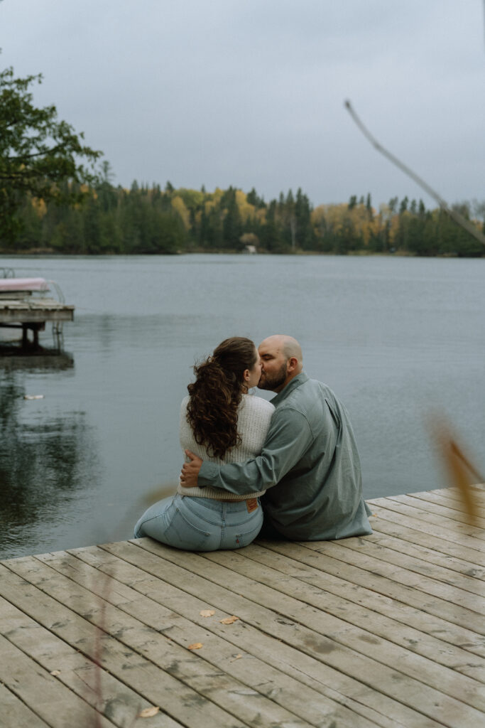 A couple kissing on the dock during an engagement session on the hunt lake trail in Manitoba