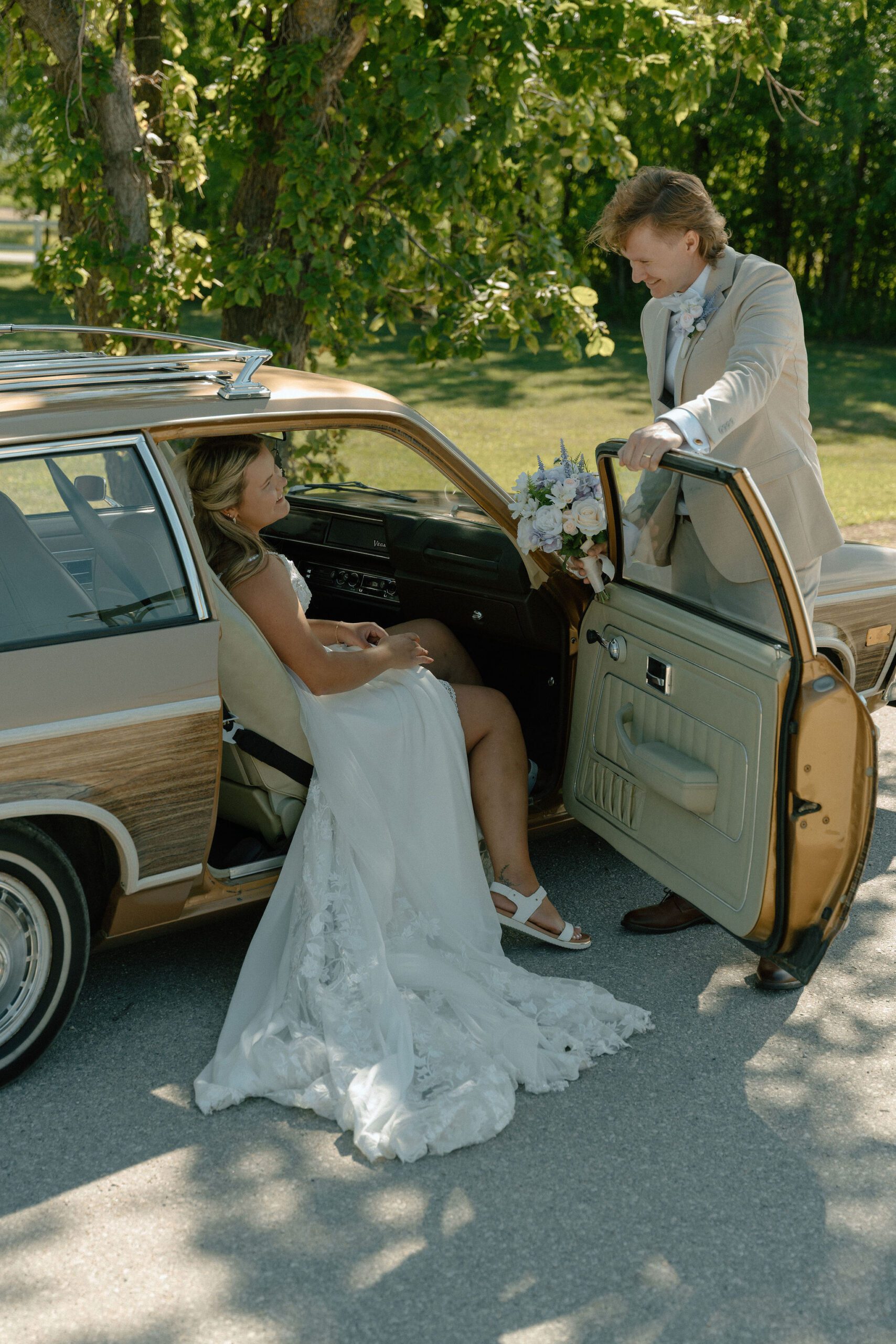 Wedding photo of bride getting in an old school car while groom holds door open