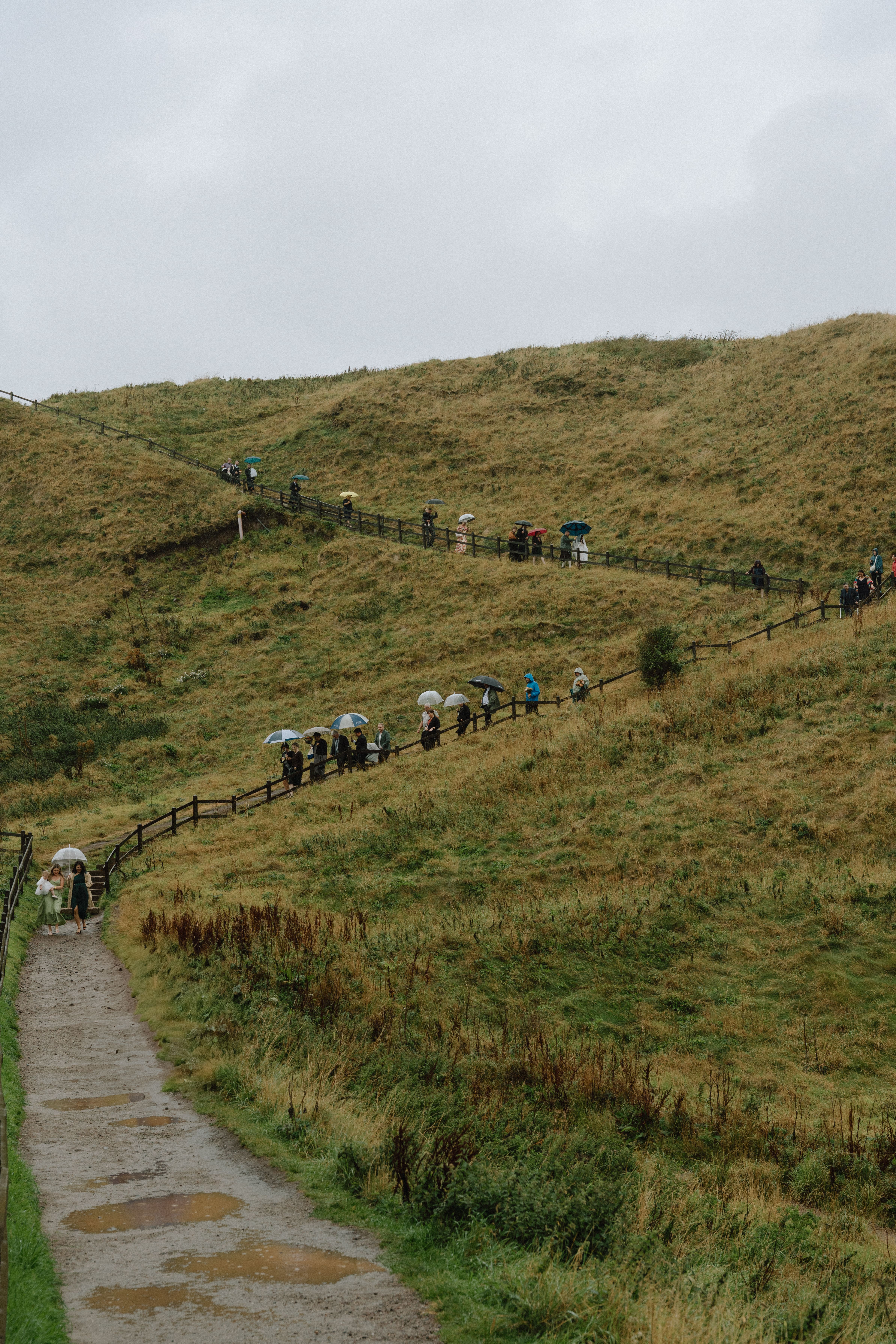 processional walk to castle wedding ceremony in Stonehaven Scotland along mountain trail on a rainy day
