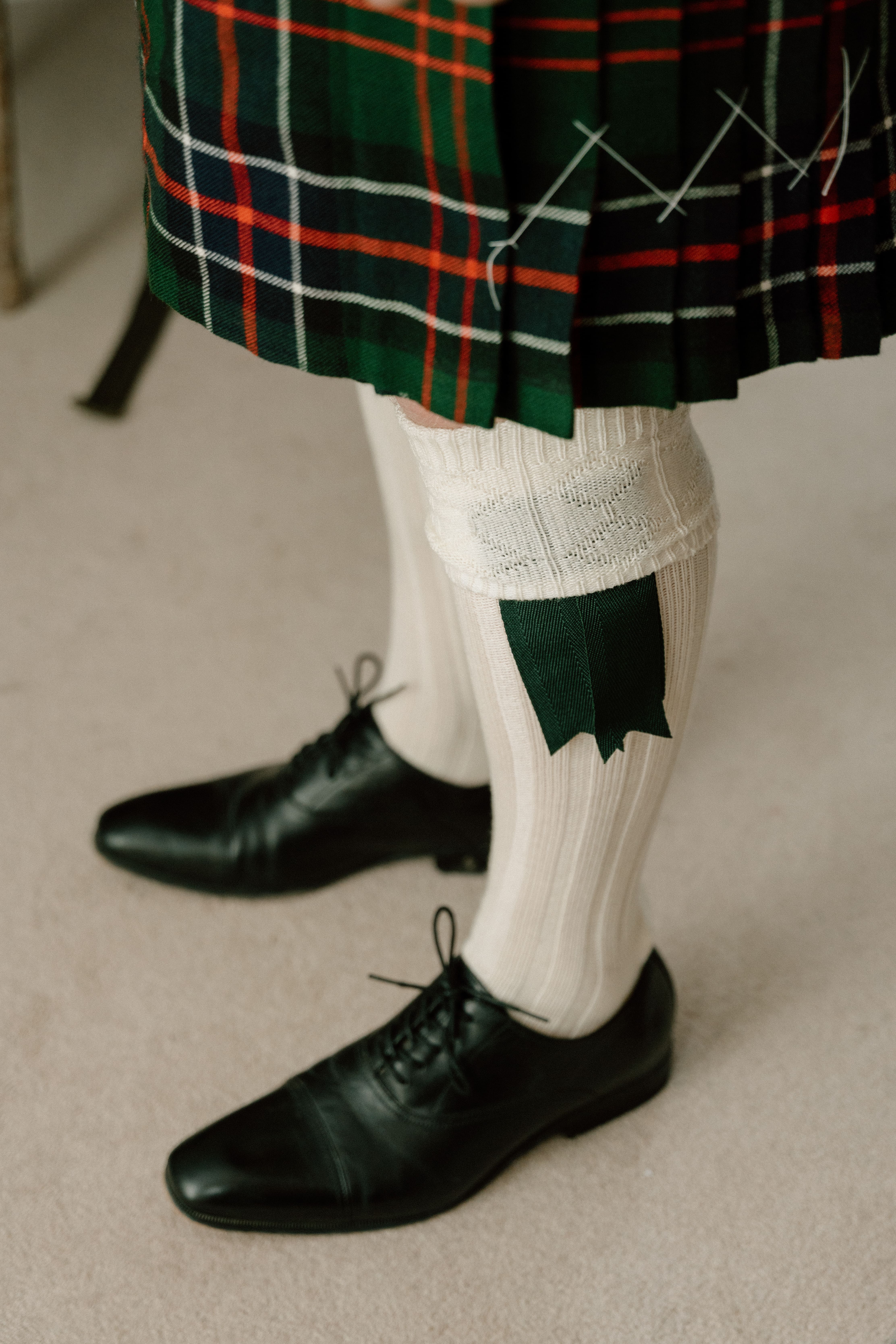 Close-up documentary wedding detail of the groom’s traditional kilt, long socks, and formal shoes during morning preparations at Elsick House in Scotland.