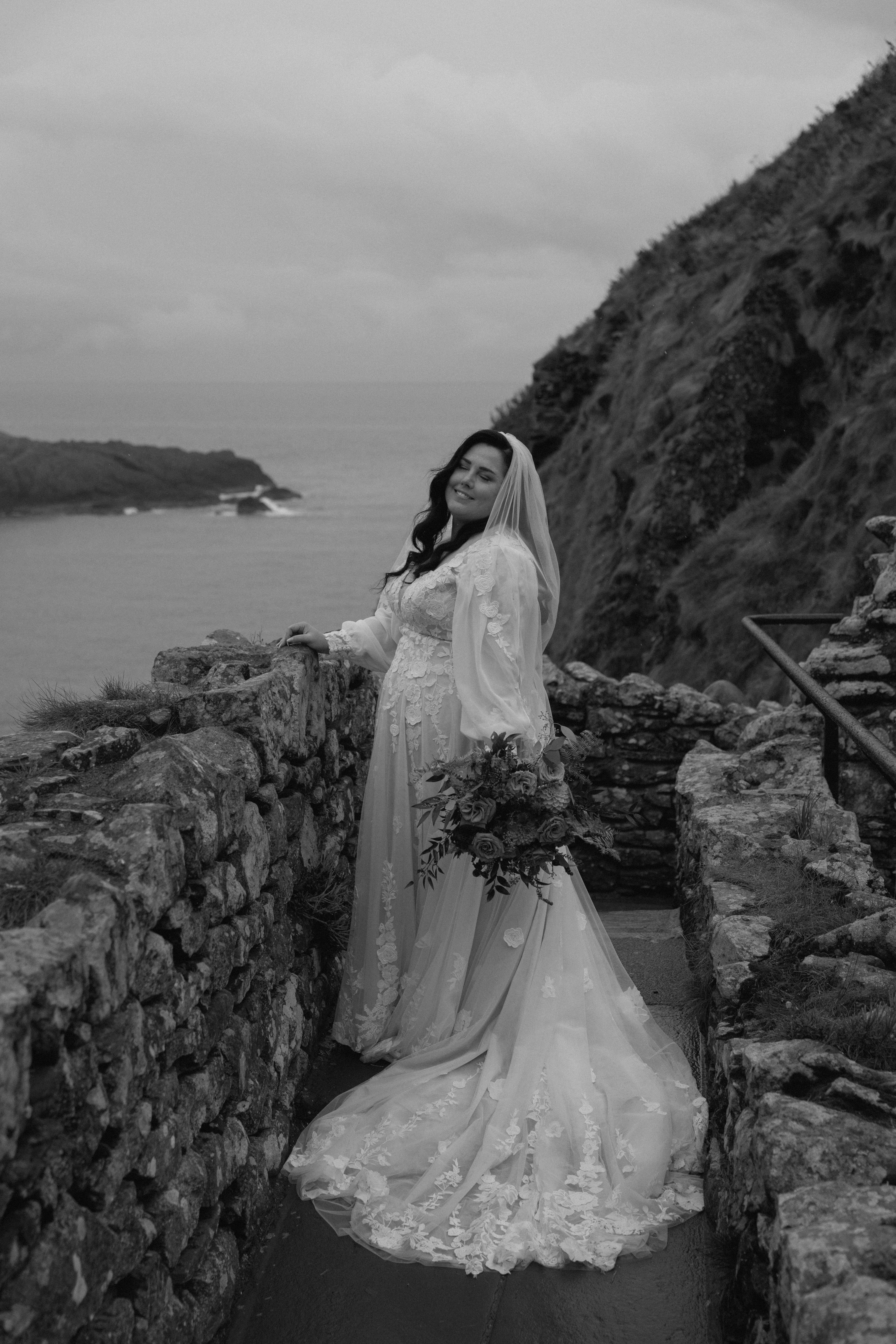 Candid bride in lace wedding dress walking on coastal trail at Dunnottar Castle, documentary mood with dramatic Scottish landscape.