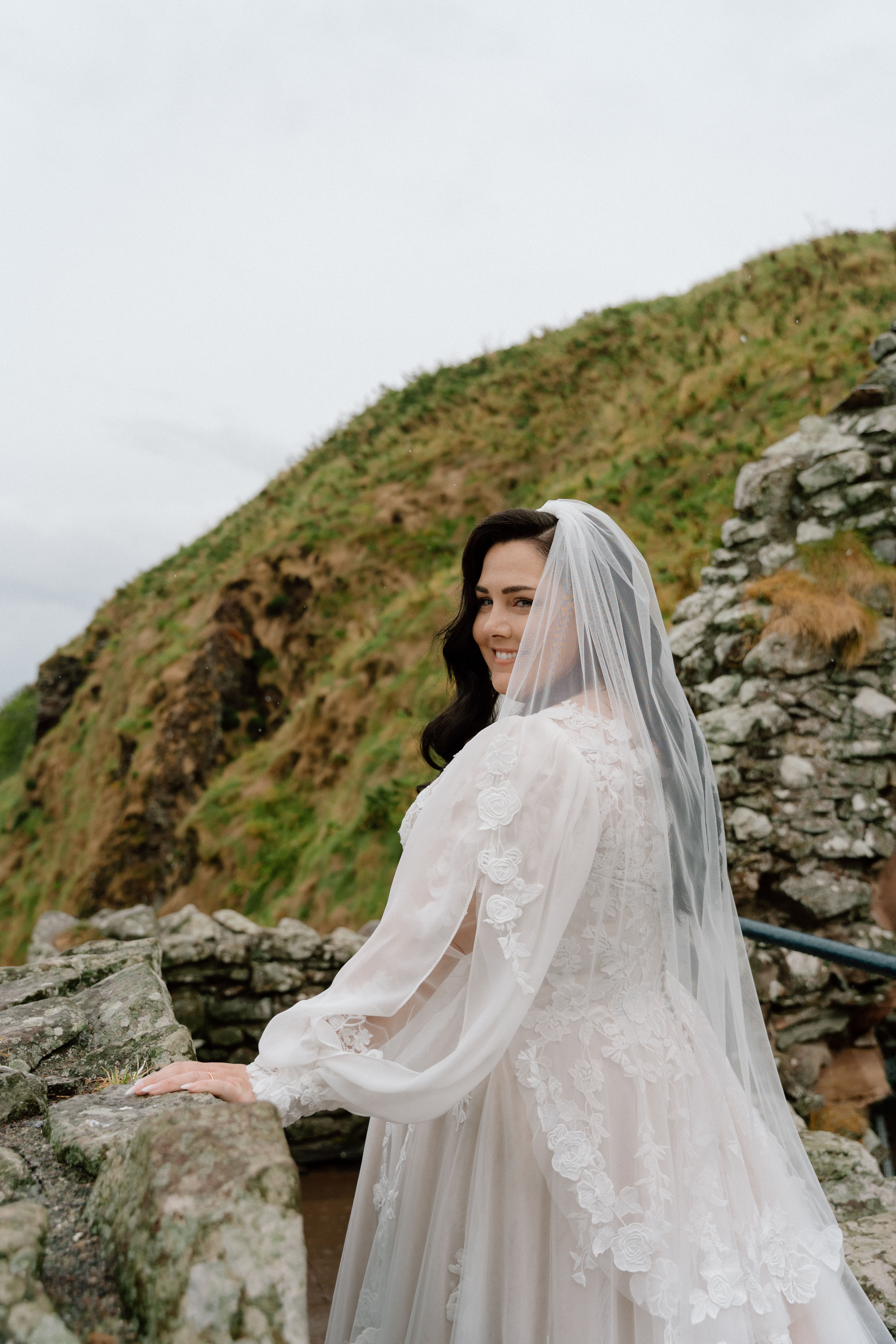 Natural wedding photography featuring Dunnottar Castle ruins and bride on rocky path, authentic candid moment Stonehaven.