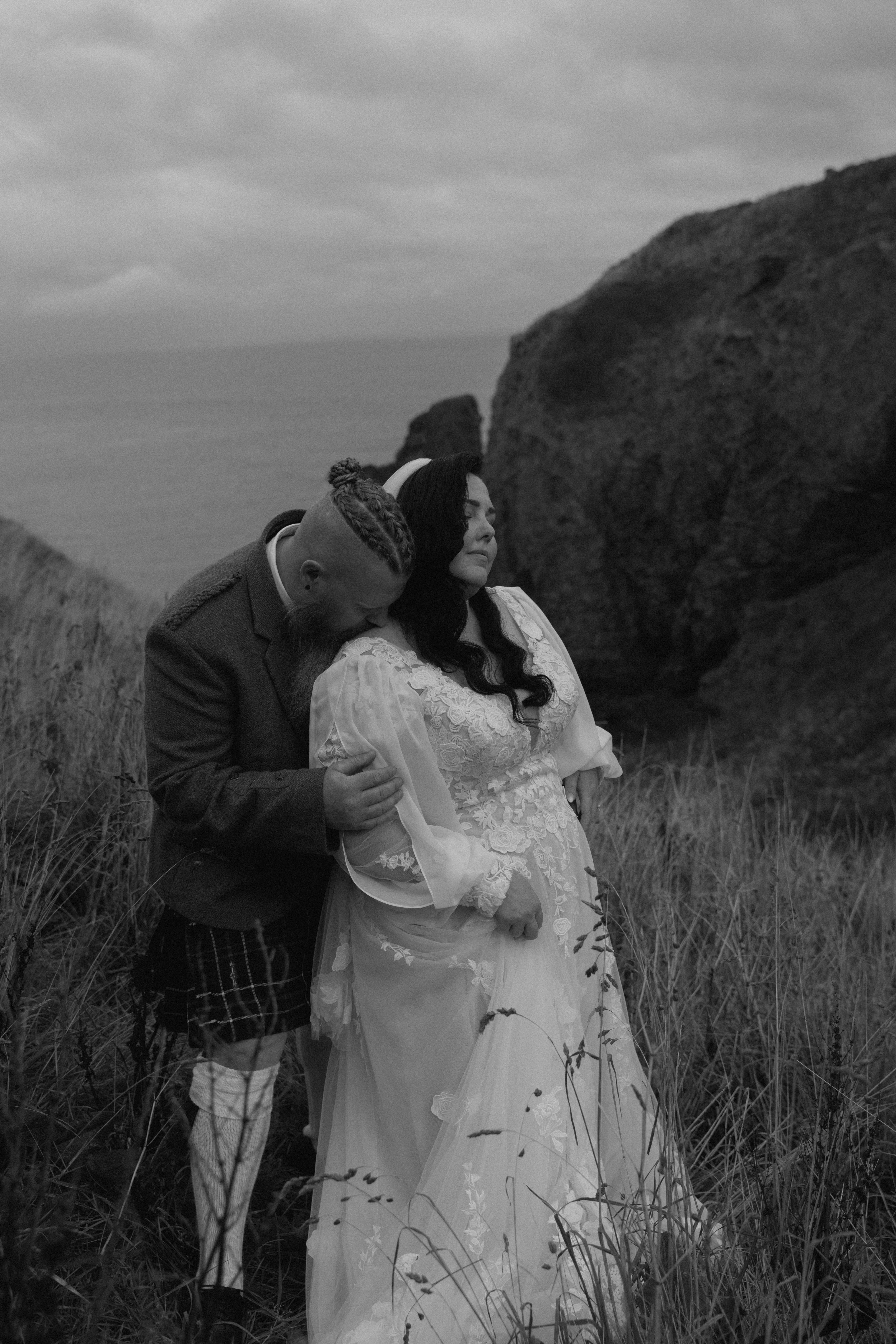 Artistic documentary wedding image of a couple embracing on rocky coastal terrain in Stonehaven with stormy skies in the background.