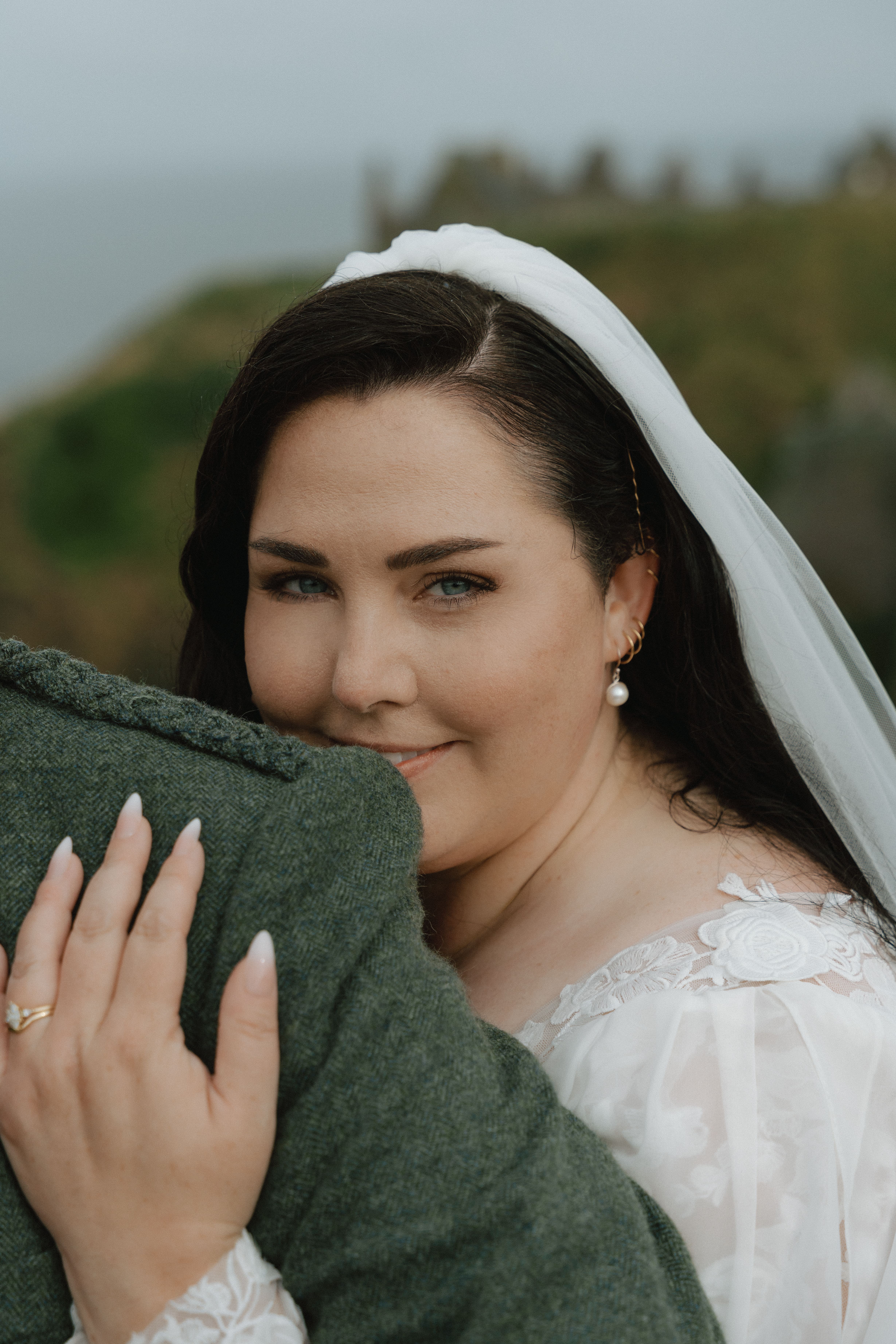Candid wedding portrait near Dunnottar Castle focusing on the bride in a natural, unposed moment with soft coastal greenery and a blurred scenic background of Dunnottar Castle.