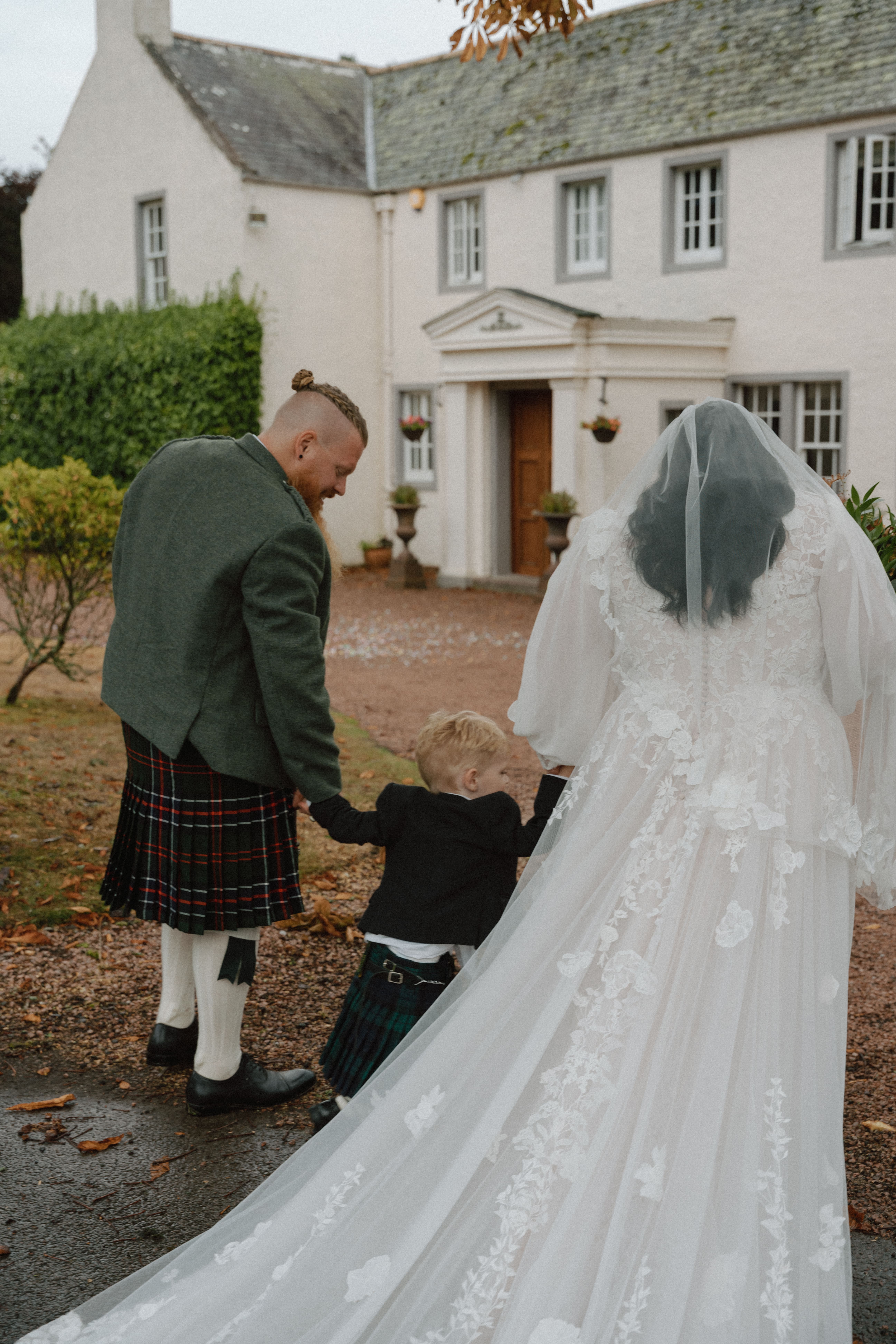 Candid family wedding photography of a couple with their child walking back to Elsick House near Dunnottar Castle in Scotland.