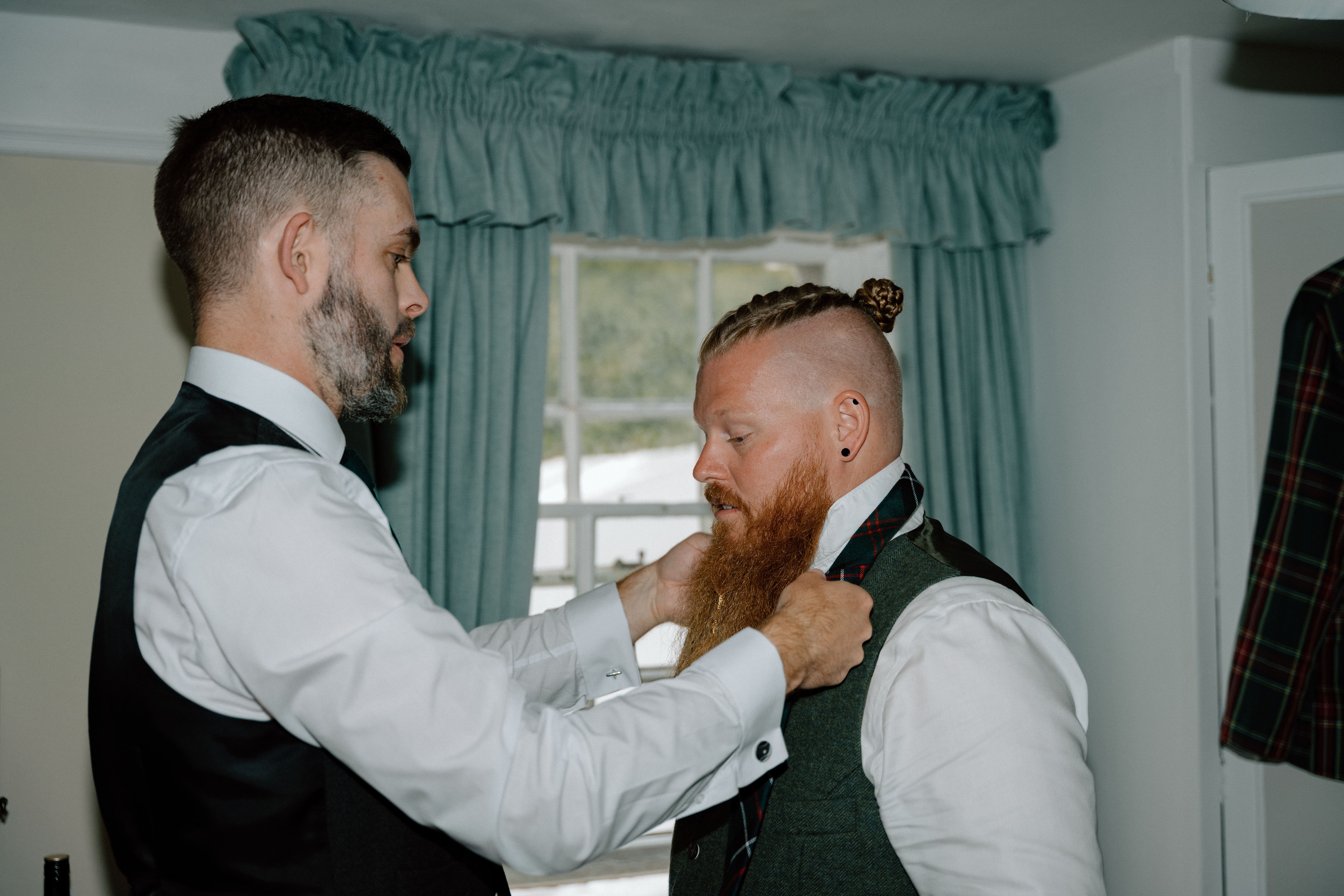 Natural documentary wedding portrait of the groom and groomsmen helping each other with ties and jackets during wedding preparations in Stonehaven, Scotland.