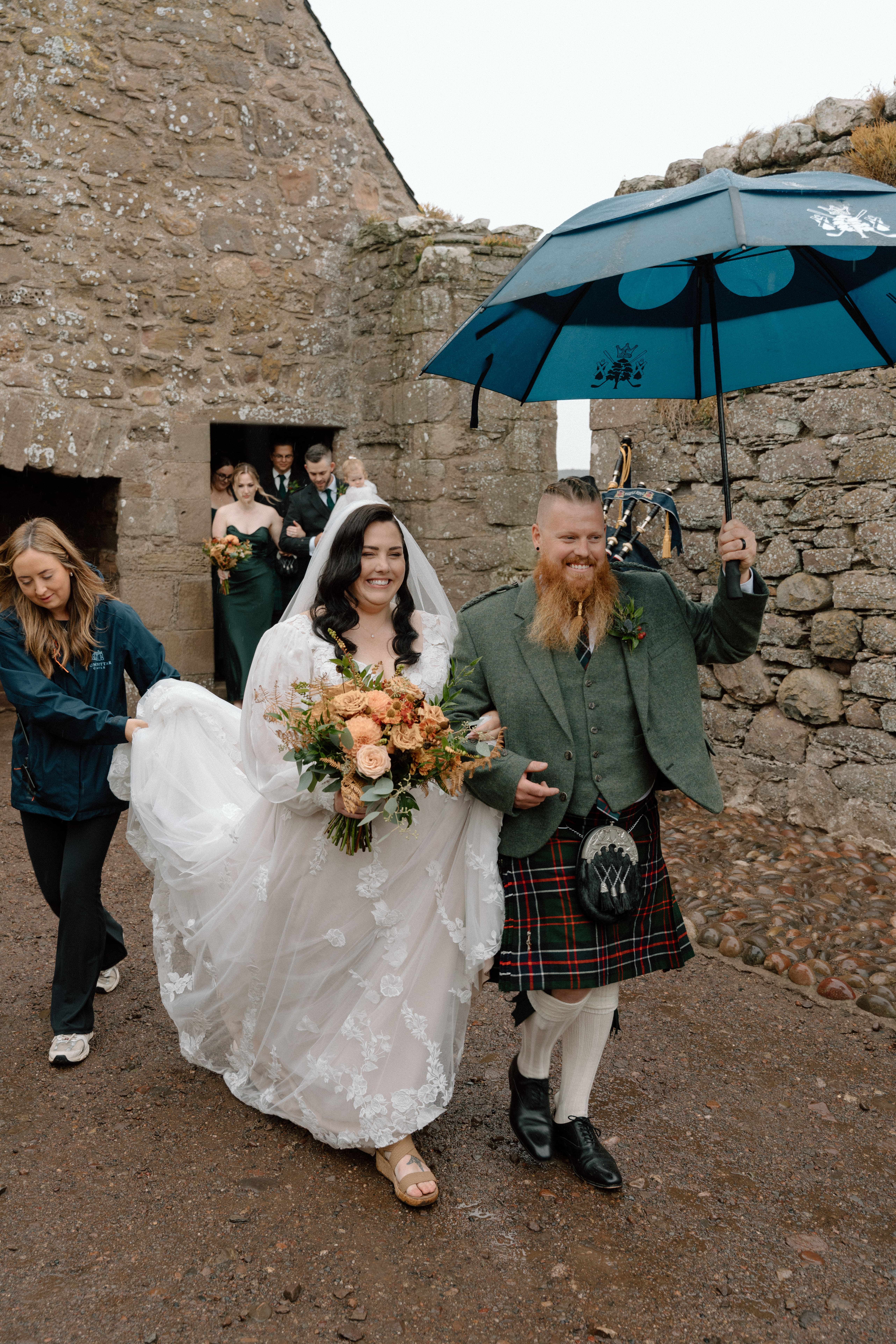 newlyweds exiting Dunnottar Castle ceremony with umbrellas and smiling guests