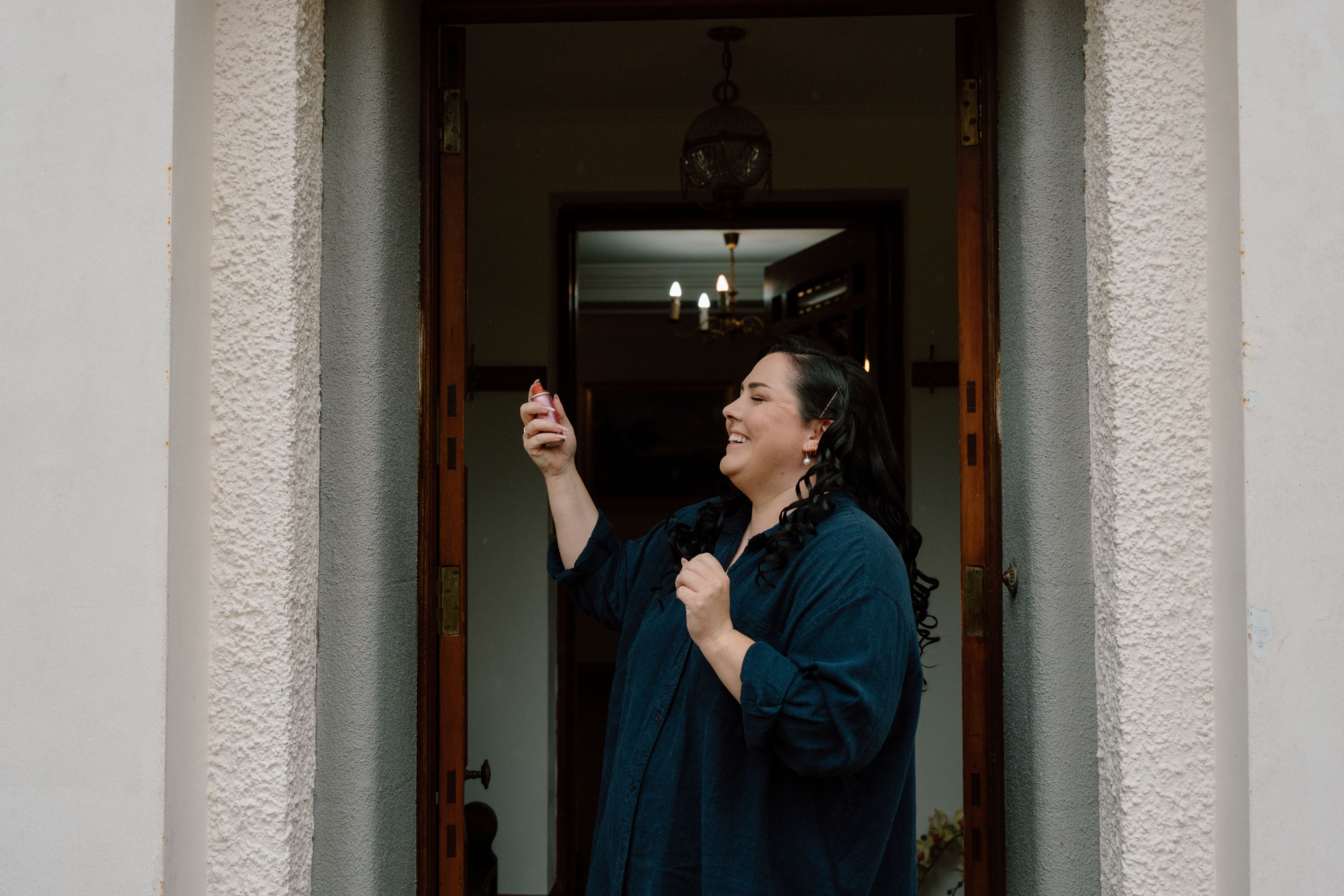 Natural wedding morning portrait of the bride applying perfume on herself outside the room during quiet pre-ceremony moments in Scotland.