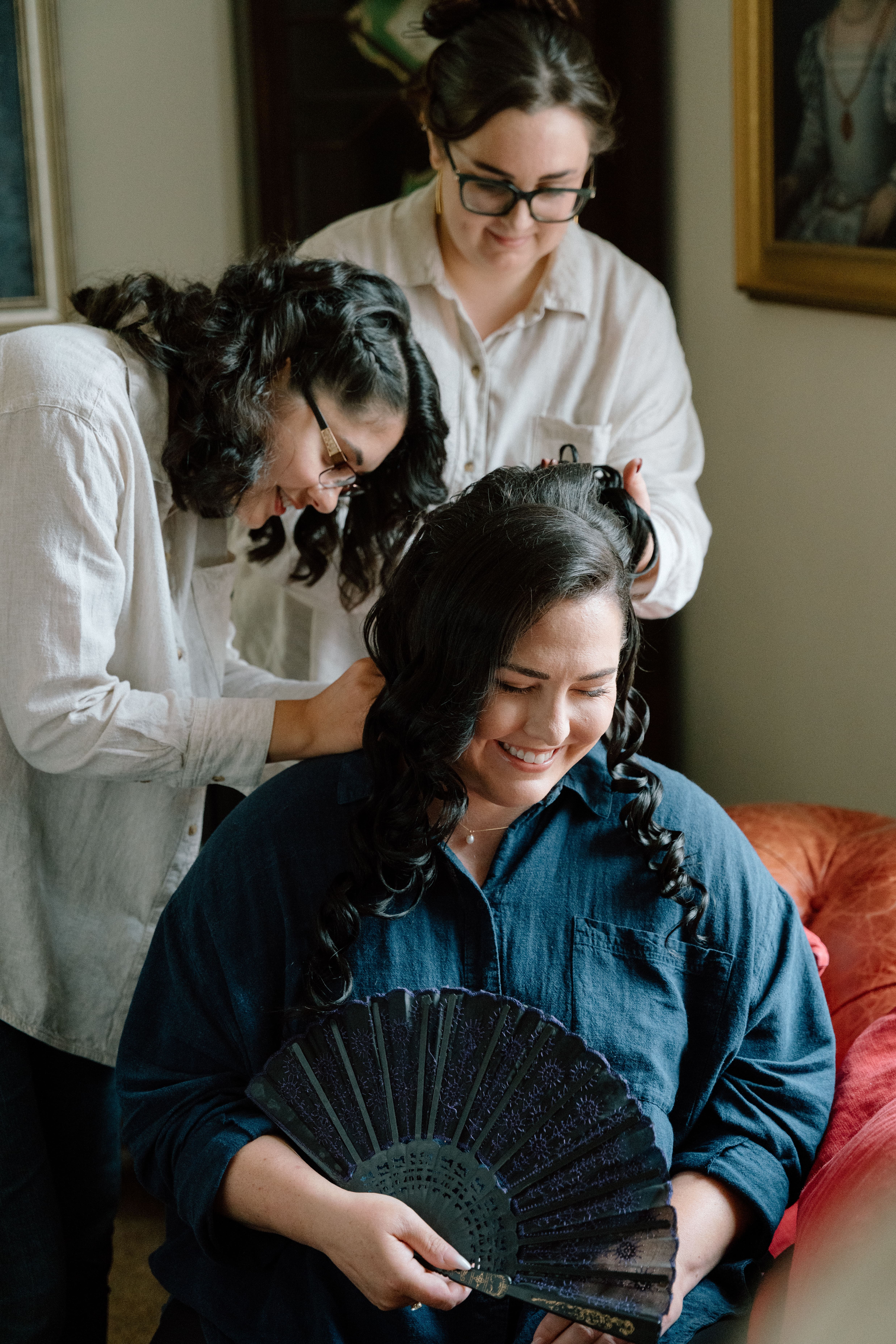Documentary-style bridal preparation image showing the bride smiling while bridesmaids help get ready during a natural wedding morning in Scotland.