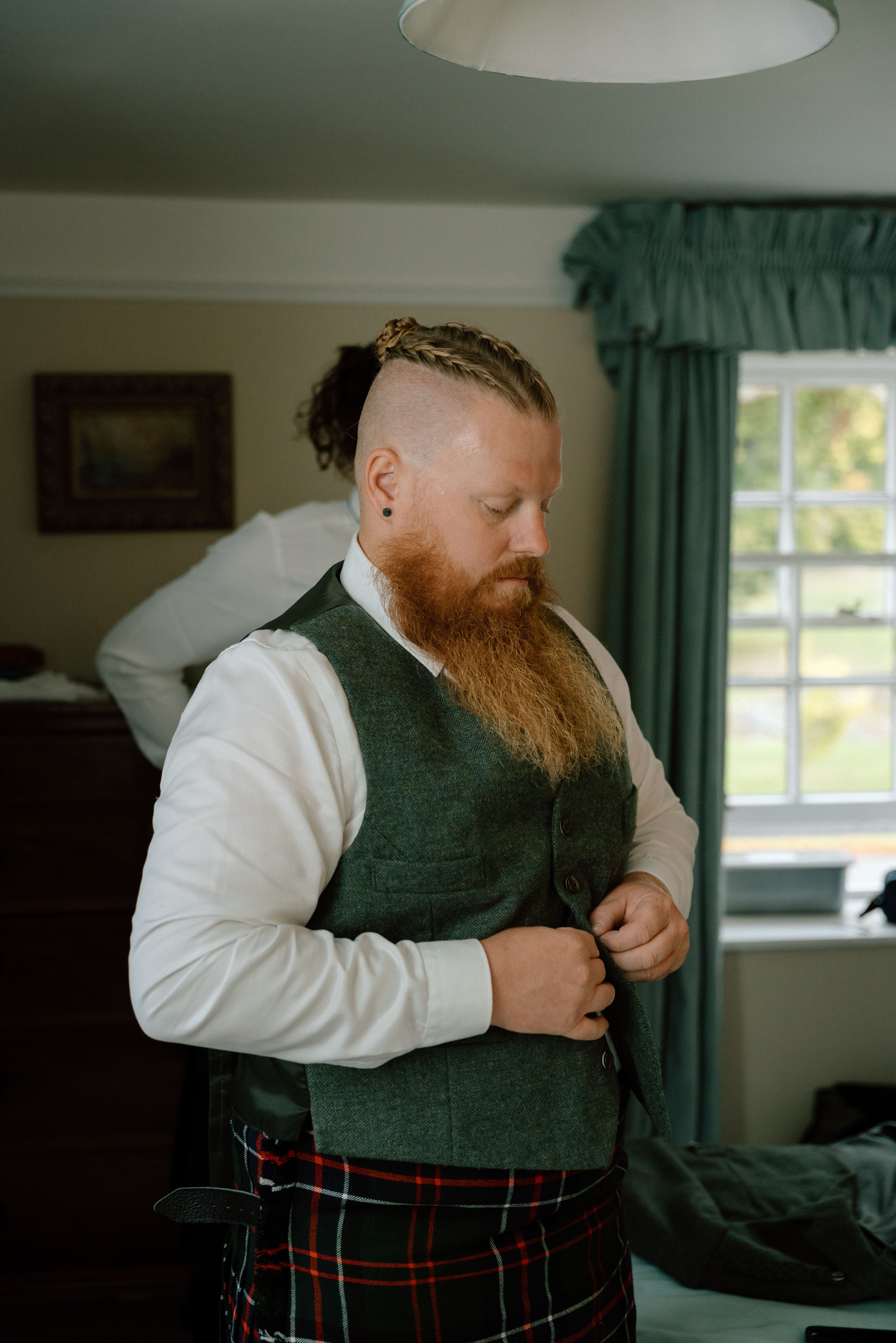 Portrait documentary wedding photo of the groom buttoning his wedding vest during morning preparations at Elsick House in a natural, candid style.