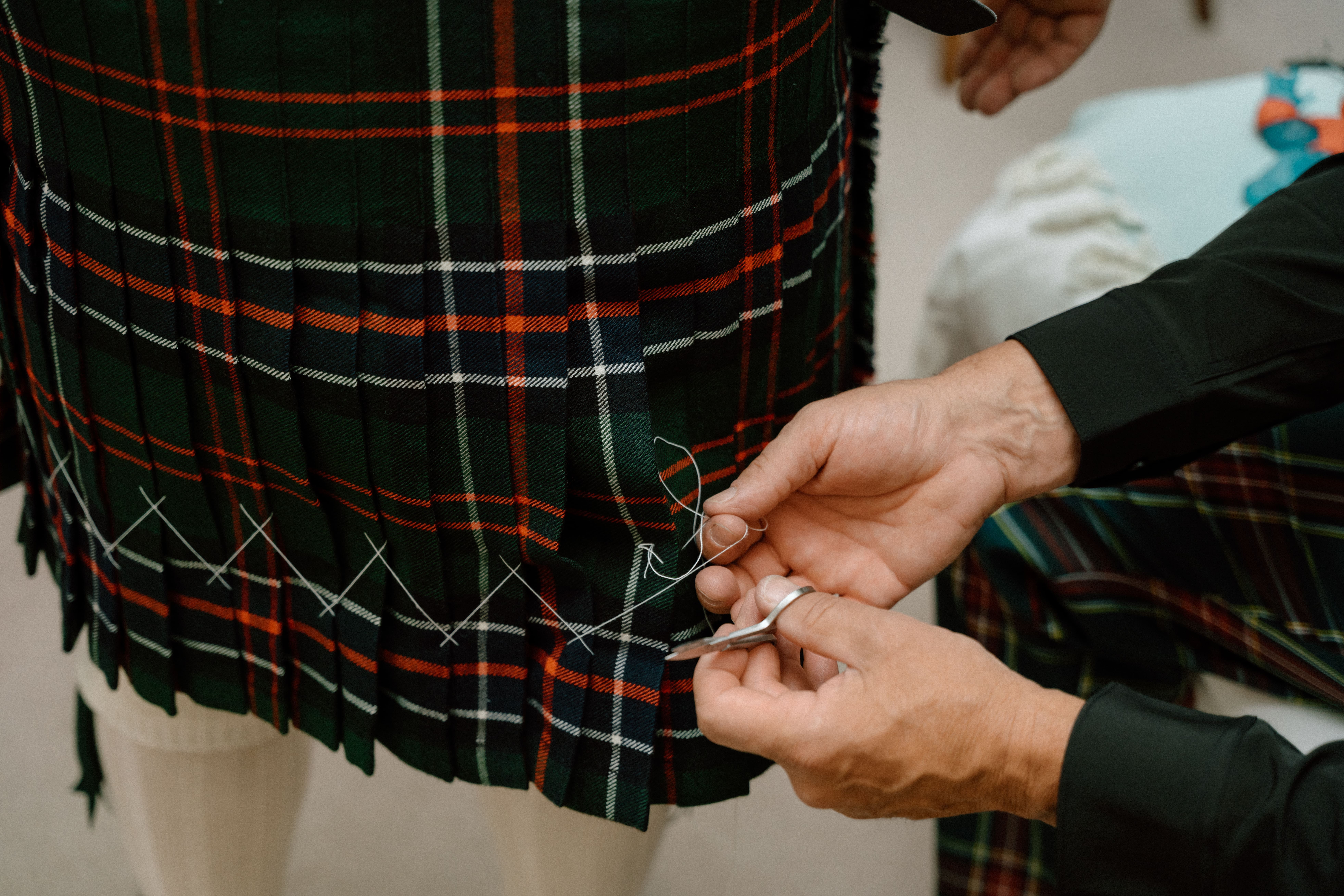 Intimate documentary wedding image of a kilt being carefully hand-stitched, capturing craftsmanship and tradition during wedding preparations in Scotland.