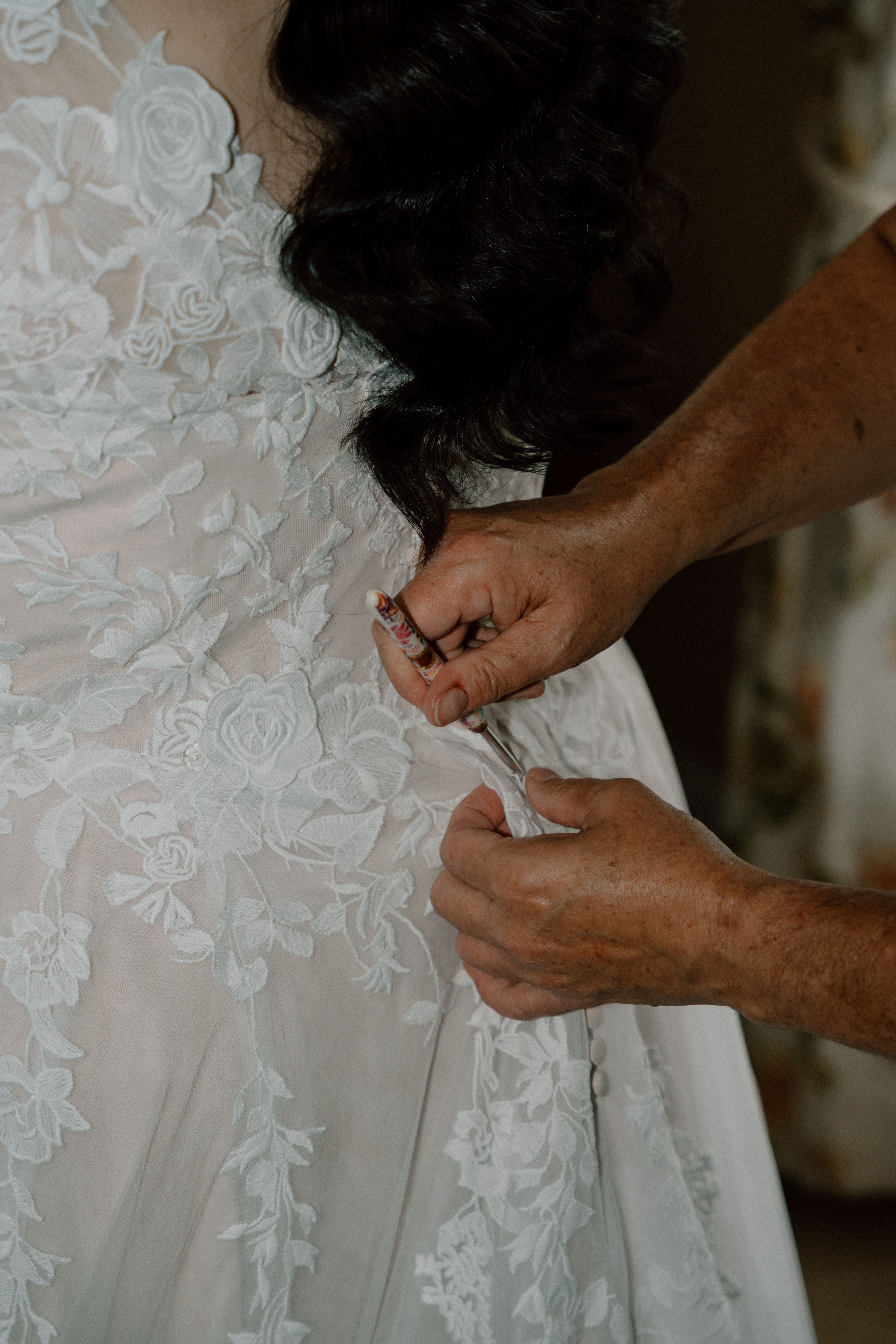 Close-up of candid wedding photography of the bride’s mother fastening the back of the wedding gown during intimate preparations in Scotland.