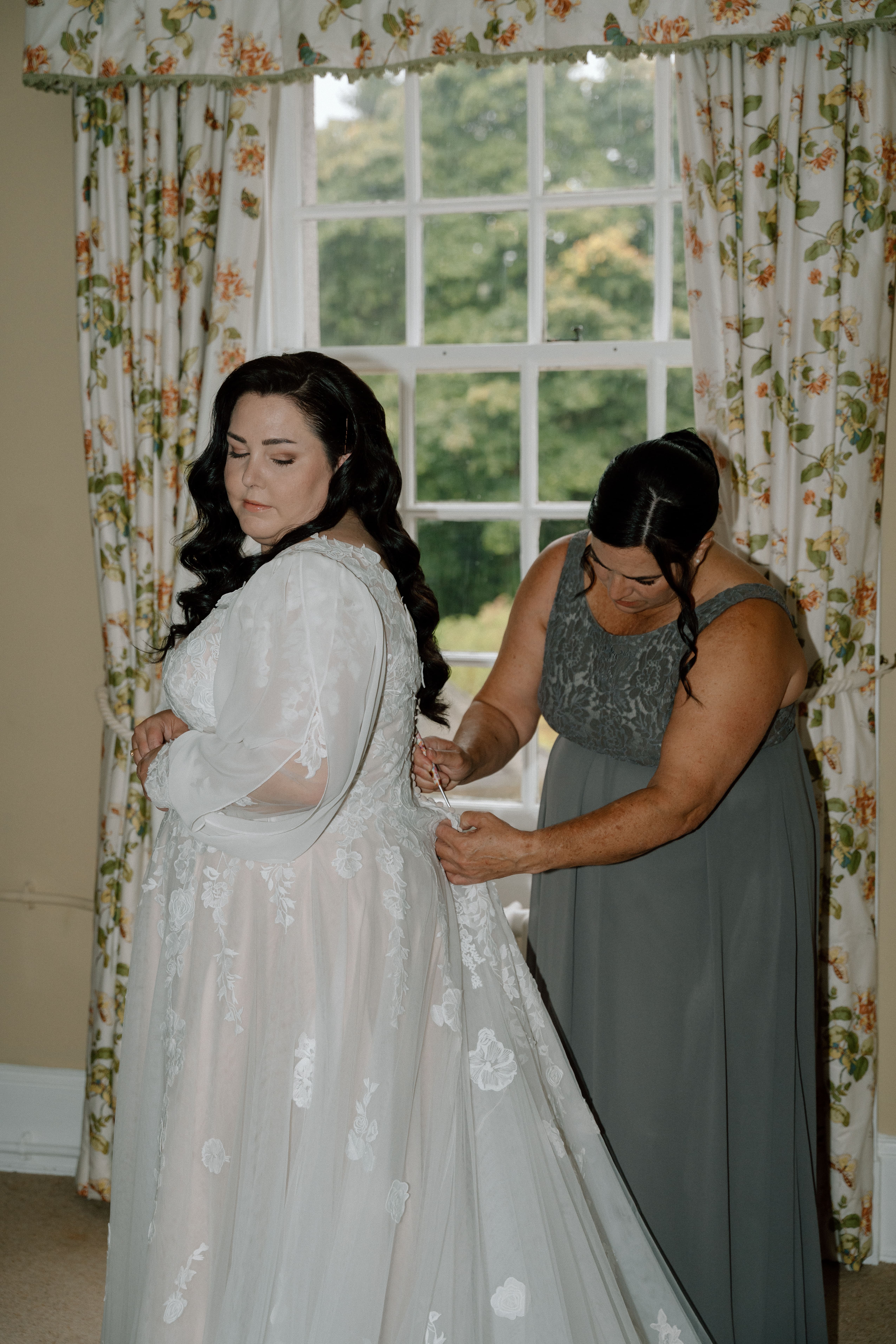 Natural documentary wedding photography of the bride’s mother fastening the back of the wedding gown during intimate preparations in Scotland.