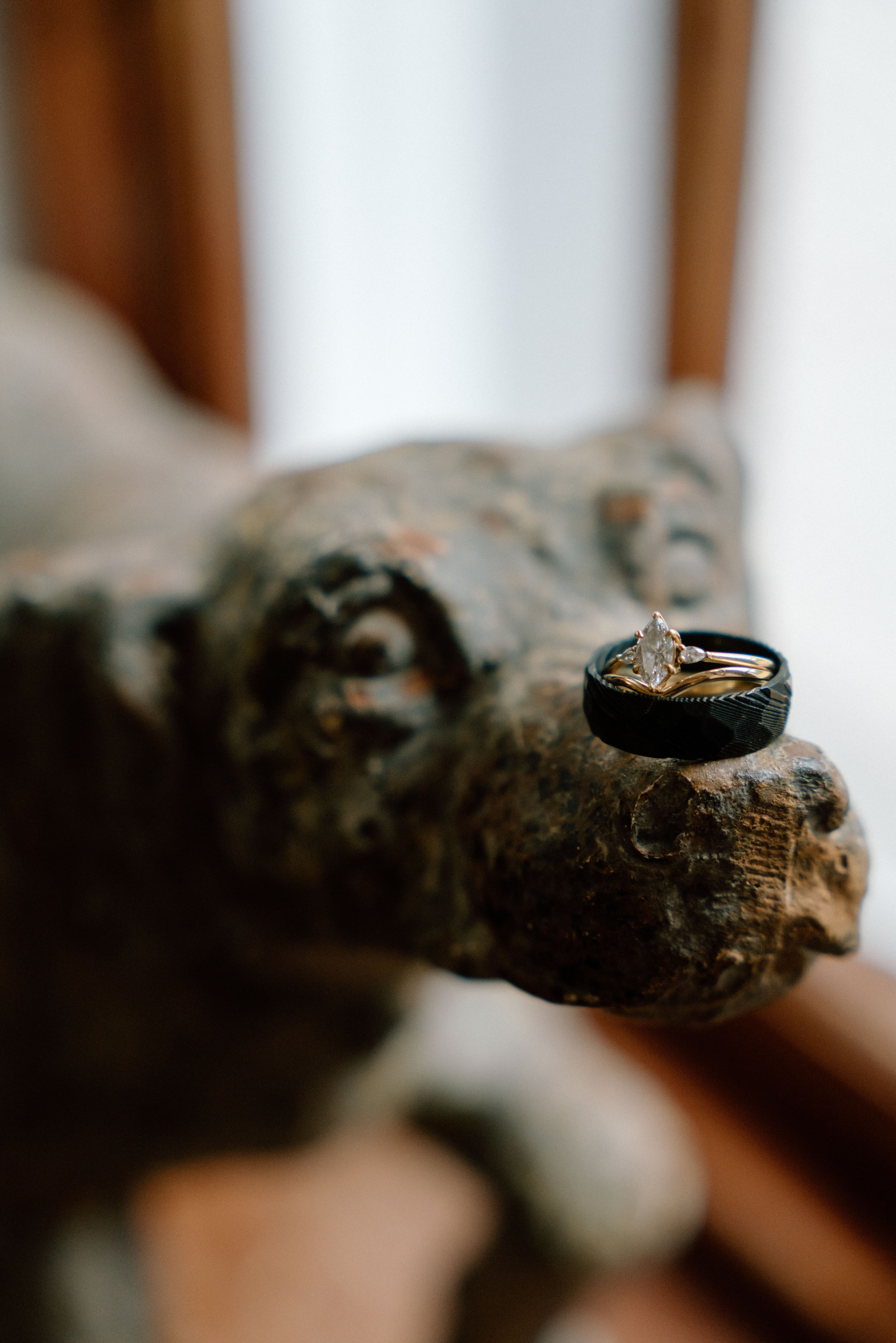 Fine art wedding photography close-up of wedding rings and groom’s ring on a decorative sculpture, captured in a styled documentary wedding moment at Elsick House.