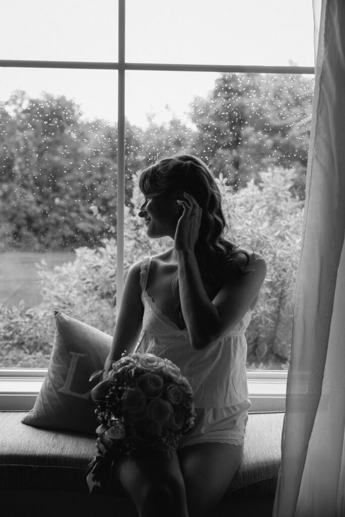 Timeless black and white bridal portrait of a bride holding her bouquet beside a window