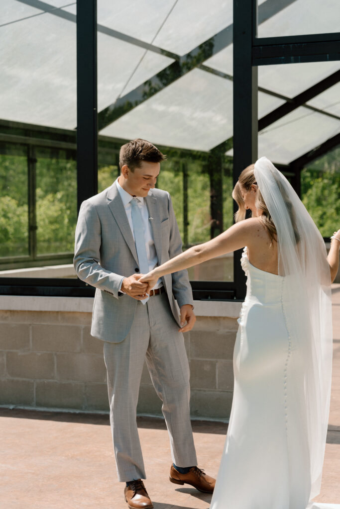 Bride and groom appreciating bride's wedding dress after their first look in front of a glass building at The White Poplar in Manitoba