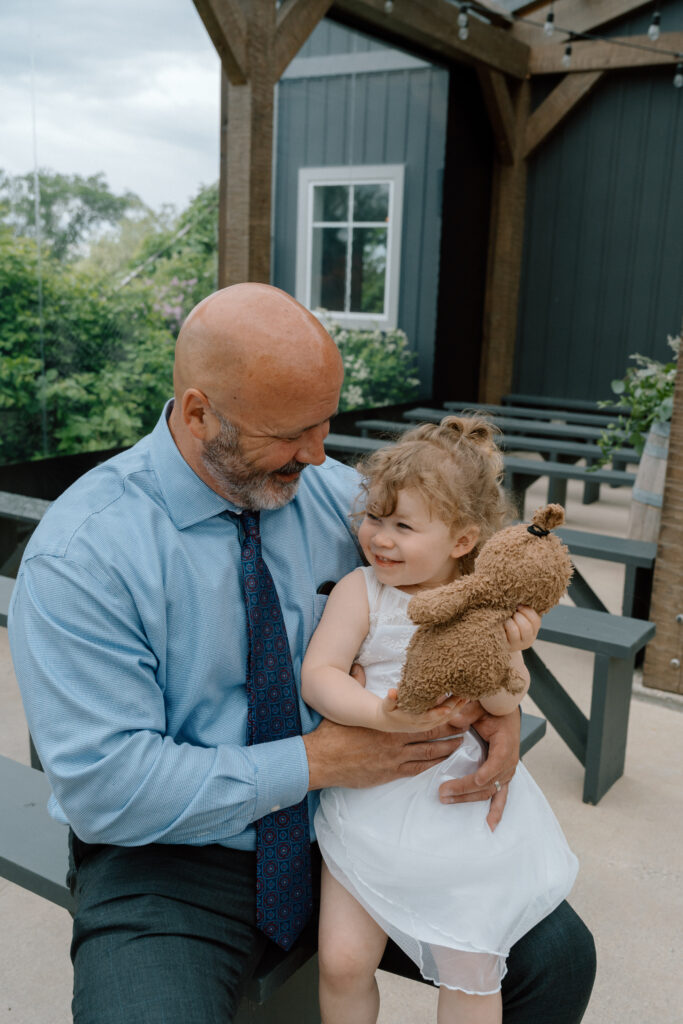 Grandfather holding a young flower girl in a white dress with her teddy bear