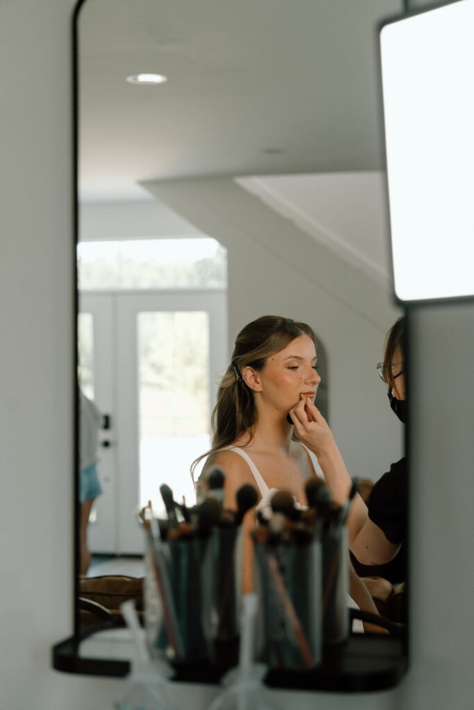 Julianna having her makeup applied through a mirror reflection during her wedding morning at The White Poplar