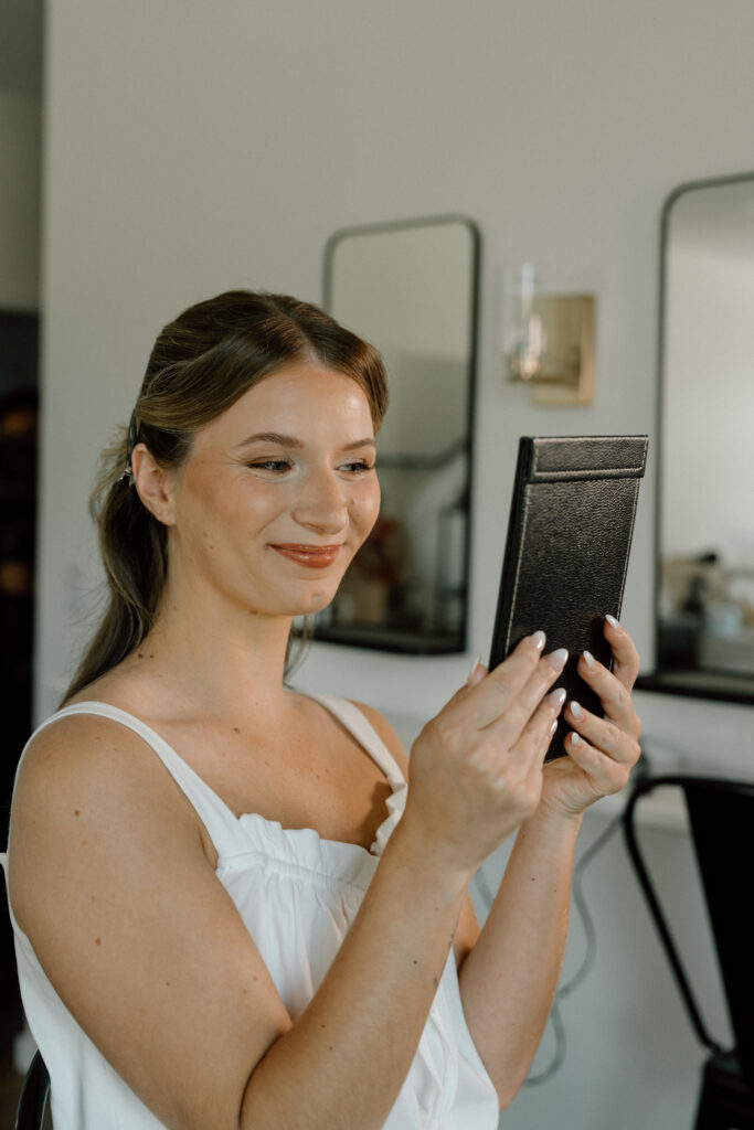 Julianna admiring her reflection in a handheld mirror during a timeless wedding morning portrait at The White Poplar
