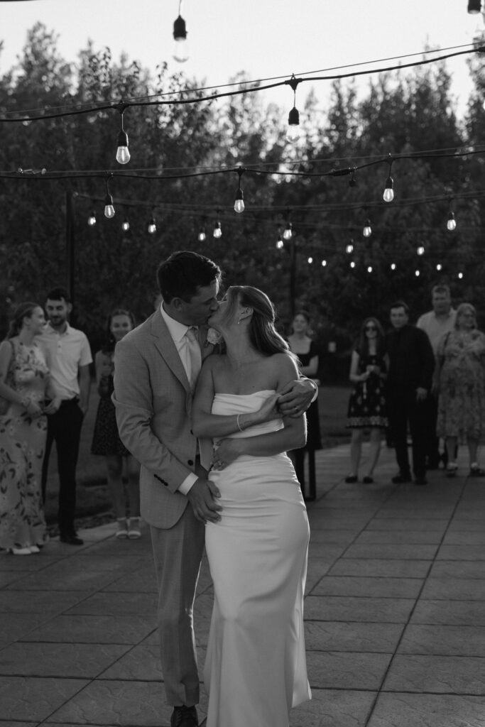 Julianna and Cole sharing a kiss during their first dance in a timeless black and white wedding photograph
