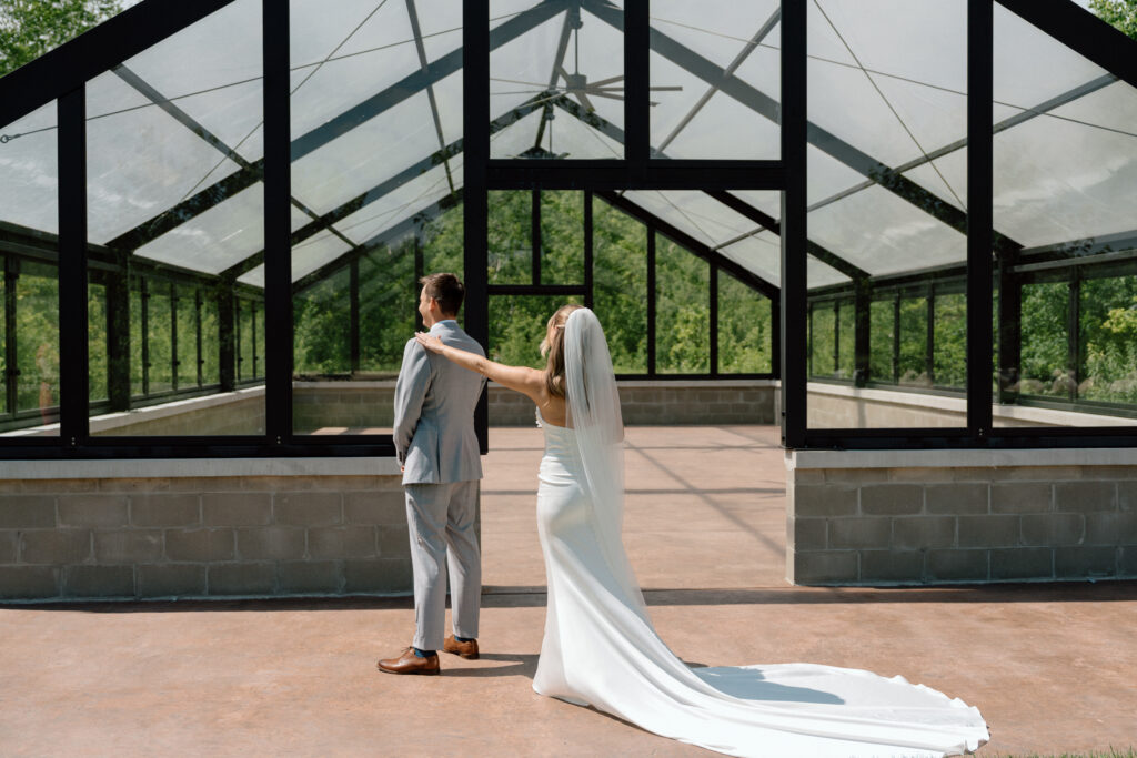 Julianna tapping Cole's shoulder for a classic first look moment in front of a glass building at The White Poplar in Manitoba