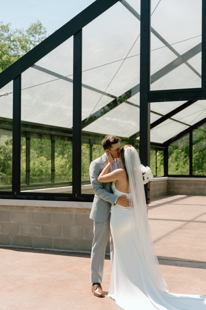 Bride and groom share a kiss in front of a glass building at The White Poplar in Manitoba