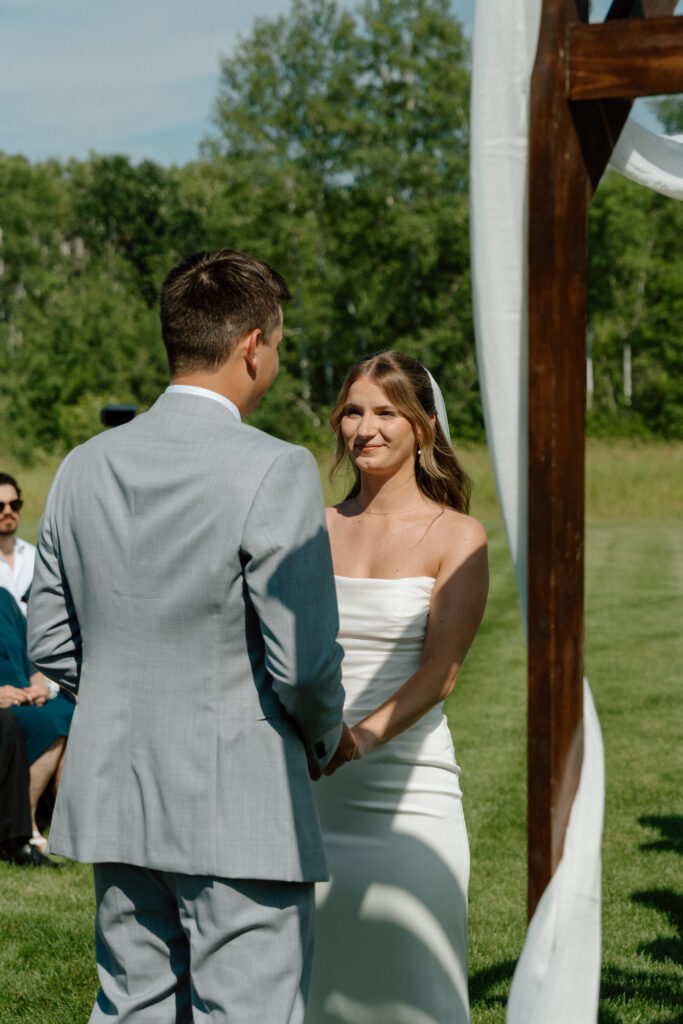 Julianna and Cole holding hands near the wooden ceremony arch during their outdoor wedding at The White Poplar