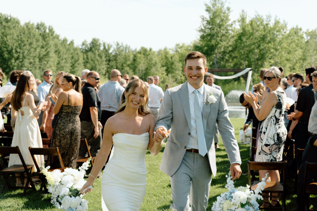 Julianna and Cole smiling and walking hand in hand after their outdoor wedding ceremony at The White Poplar