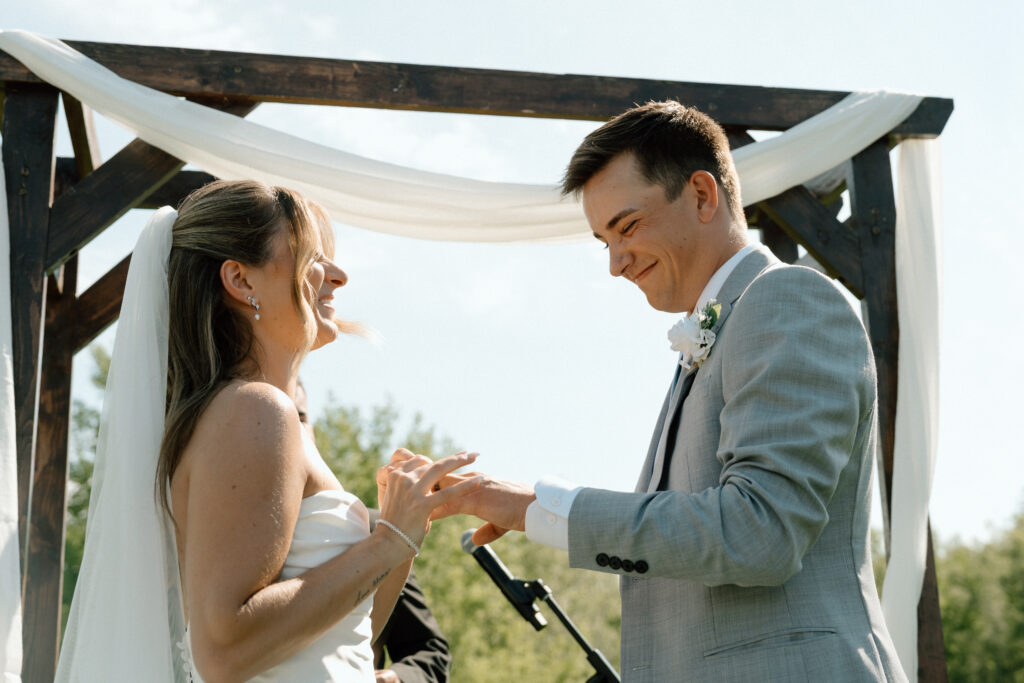 Julianna placing a wedding ring on Cole's hand during their White Poplar wedding ceremony in Manitoba