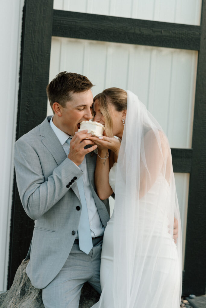 Julianna and Cole sharing their cute, small wedding cake for a candid moment at The White Poplar in Manitoba