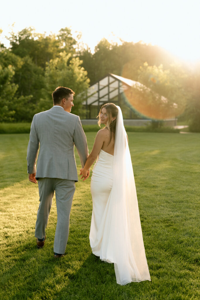 Julianna and Cole walk together across the grounds of The White Poplar during golden hour, creating a timeless and romantic wedding portrait.