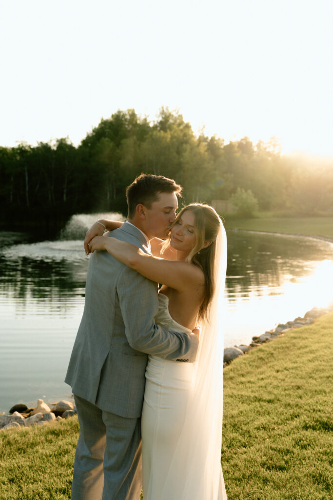 Julianna and Cole embracing in a timeless wedding portrait beside the pond at The White Poplar in Manitoba