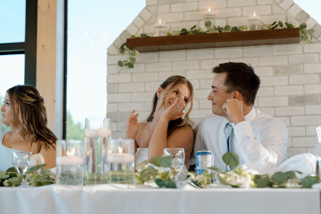 Julianna smiling and wiping away tears beside Cole during their wedding reception at The White Poplar