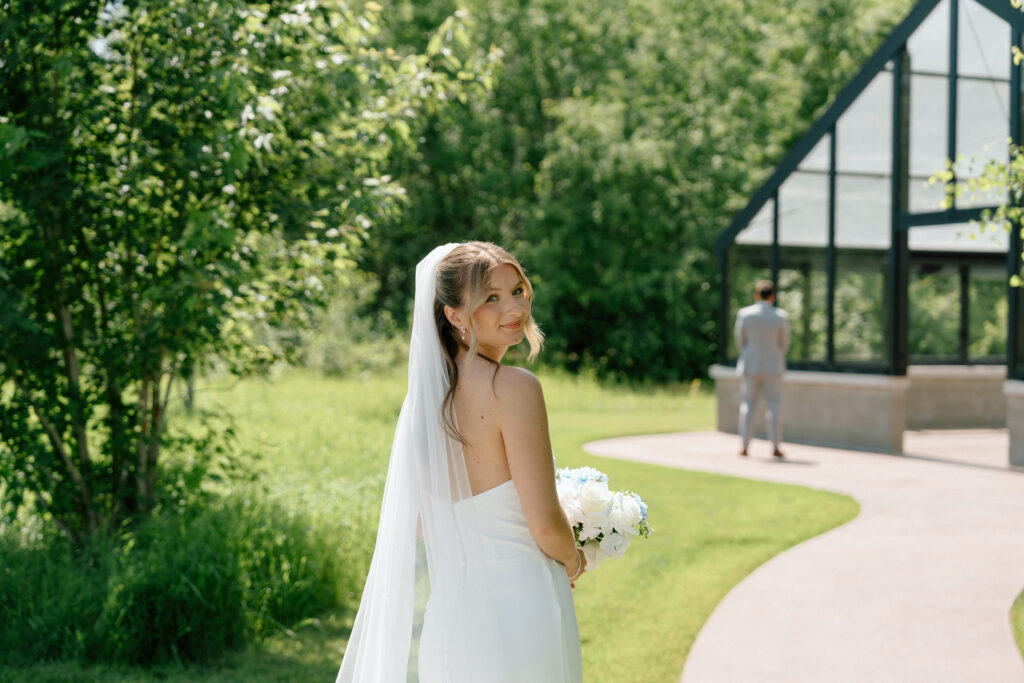 Julianna looking back at the camera before approaching the groom for their first look at The White Poplar in Manitoba