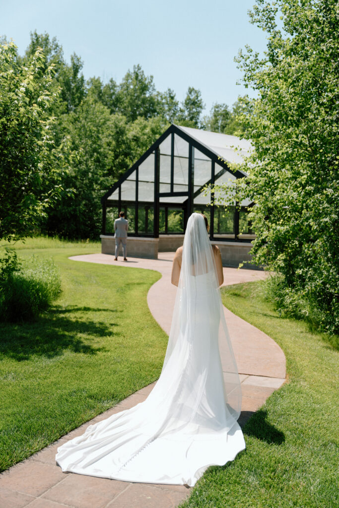 Julianna walking toward Cole with her long veil during a classic wedding portrait at The White Poplar in Manitoba