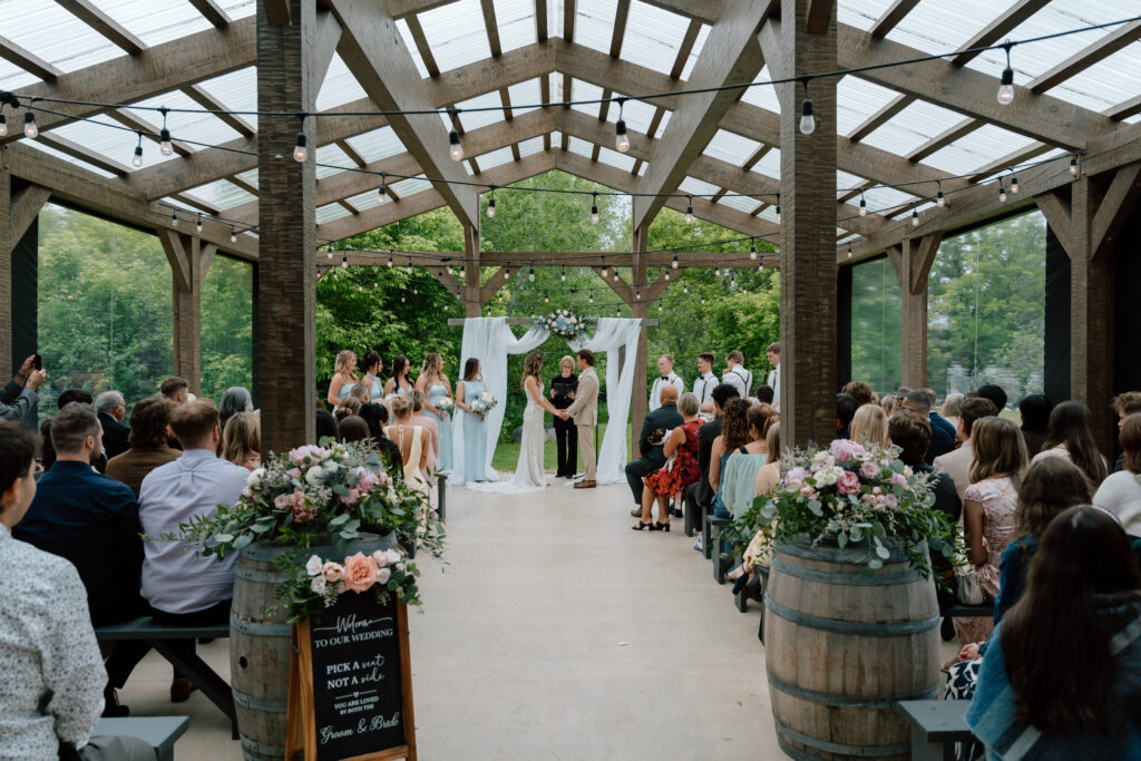 Kayla and Myles holding hands at the altar as their wedding guests watch at Hawthorne Estates in Manitoba