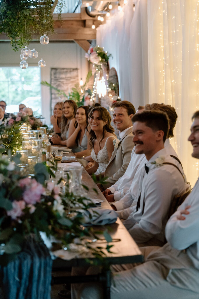 Kayla, Myles, bridesmaids and groomsmen listening to a speech during their Hawthorne Estates wedding reception