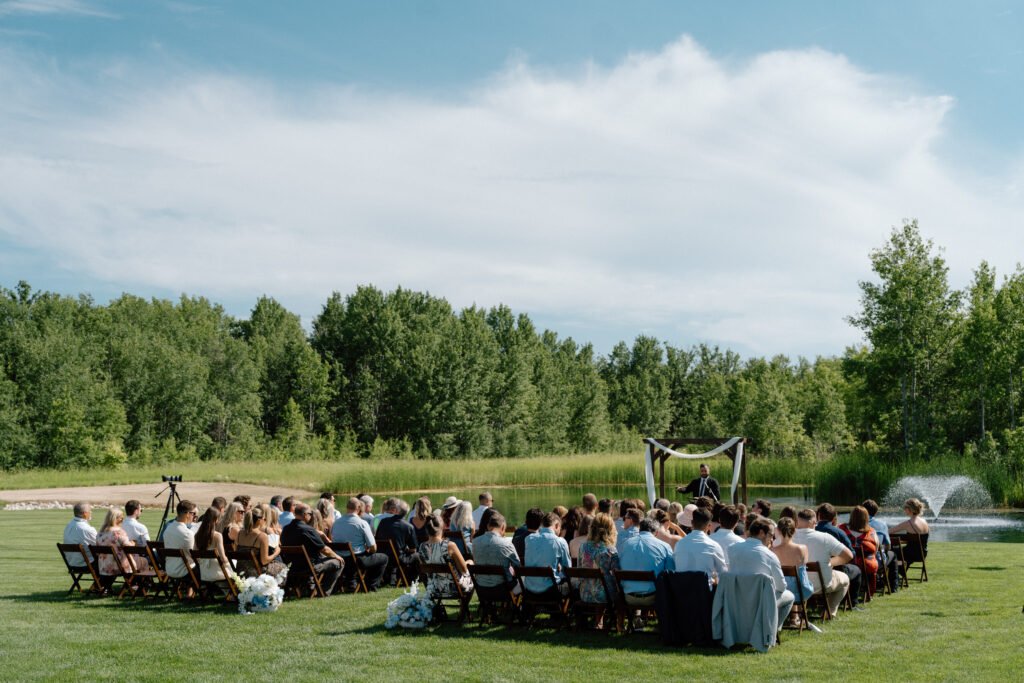 Outdoor wedding ceremony at The White Poplar surrounded by the pond, fountain, and natural Manitoba landscape