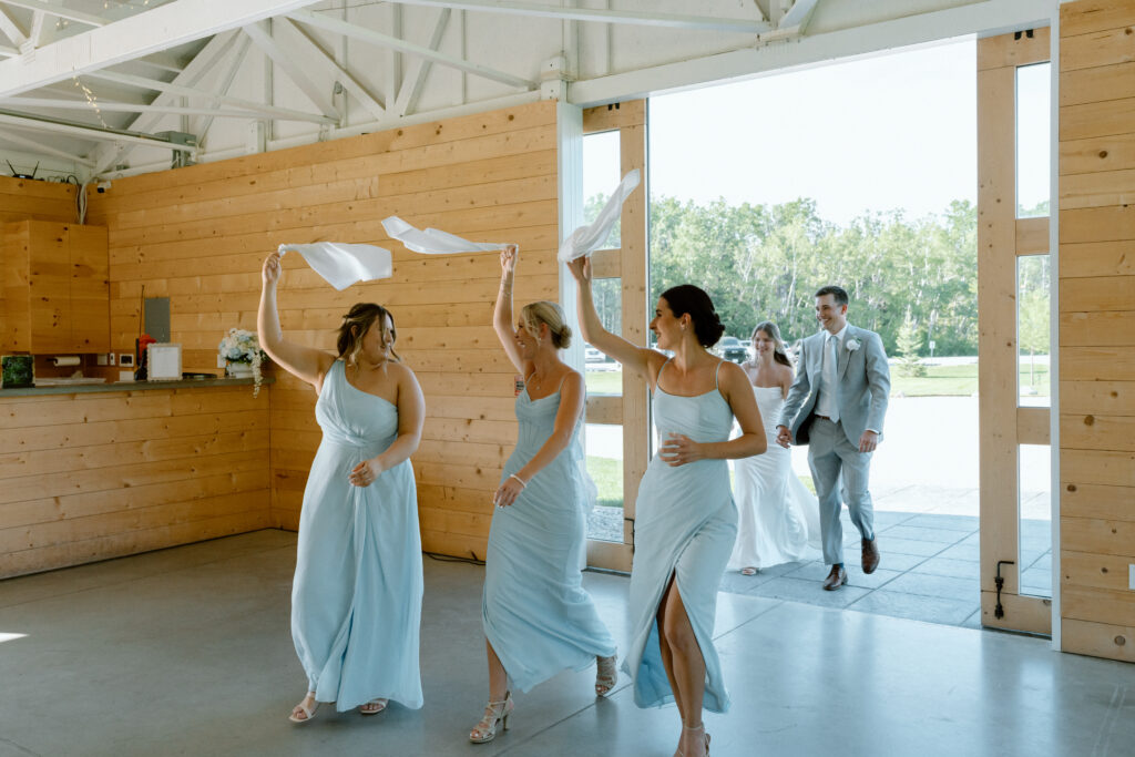 Bridesmaids laughing and waving white handkerchiefs during the wedding reception entrance at The White Poplar