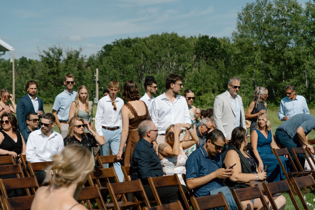 Wedding guests finding their seats on a hot day for Julianna and Cole's outdoor ceremony at The White Poplar in Manitoba