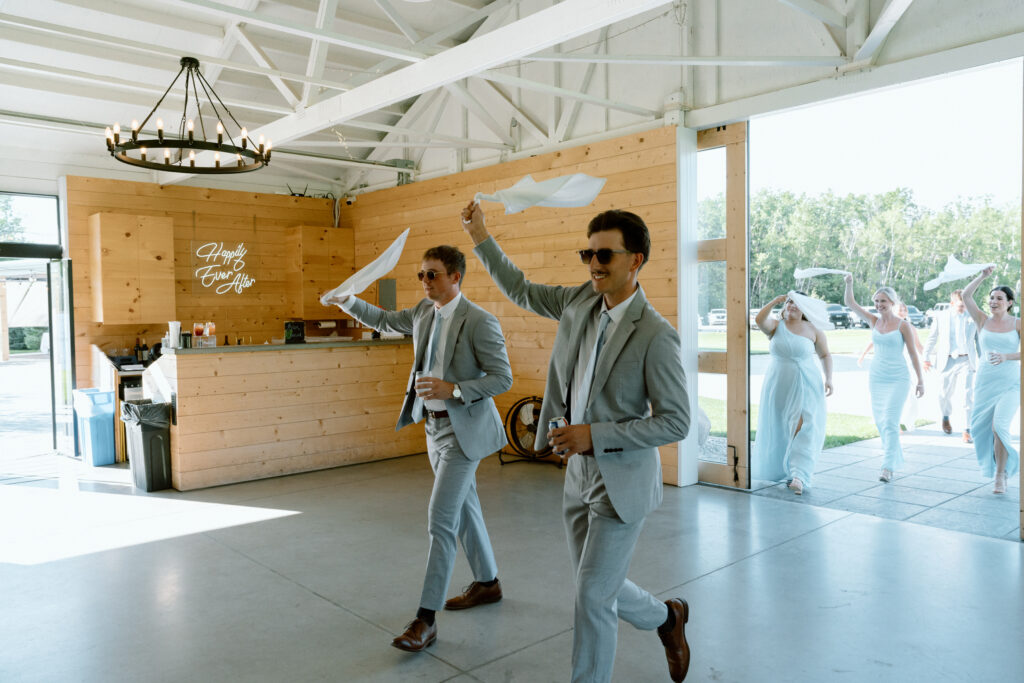 Groomsmen smiling and waving white handkerchiefs during Julianna and Cole's wedding reception entrance at The White Poplar
