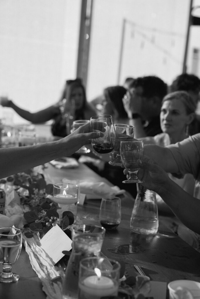 Wedding guests raising wine glasses for a toast during Julianna and Cole's reception at The White Poplar